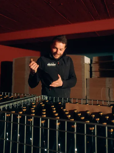 Winemaker explaining something in front of wire crates full of sparkling wine bottles