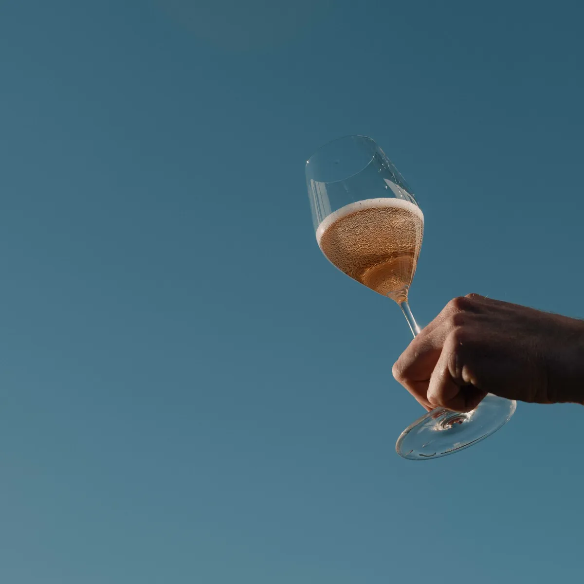 Hand holding a glass of rosé sparkling wine against a blue sky