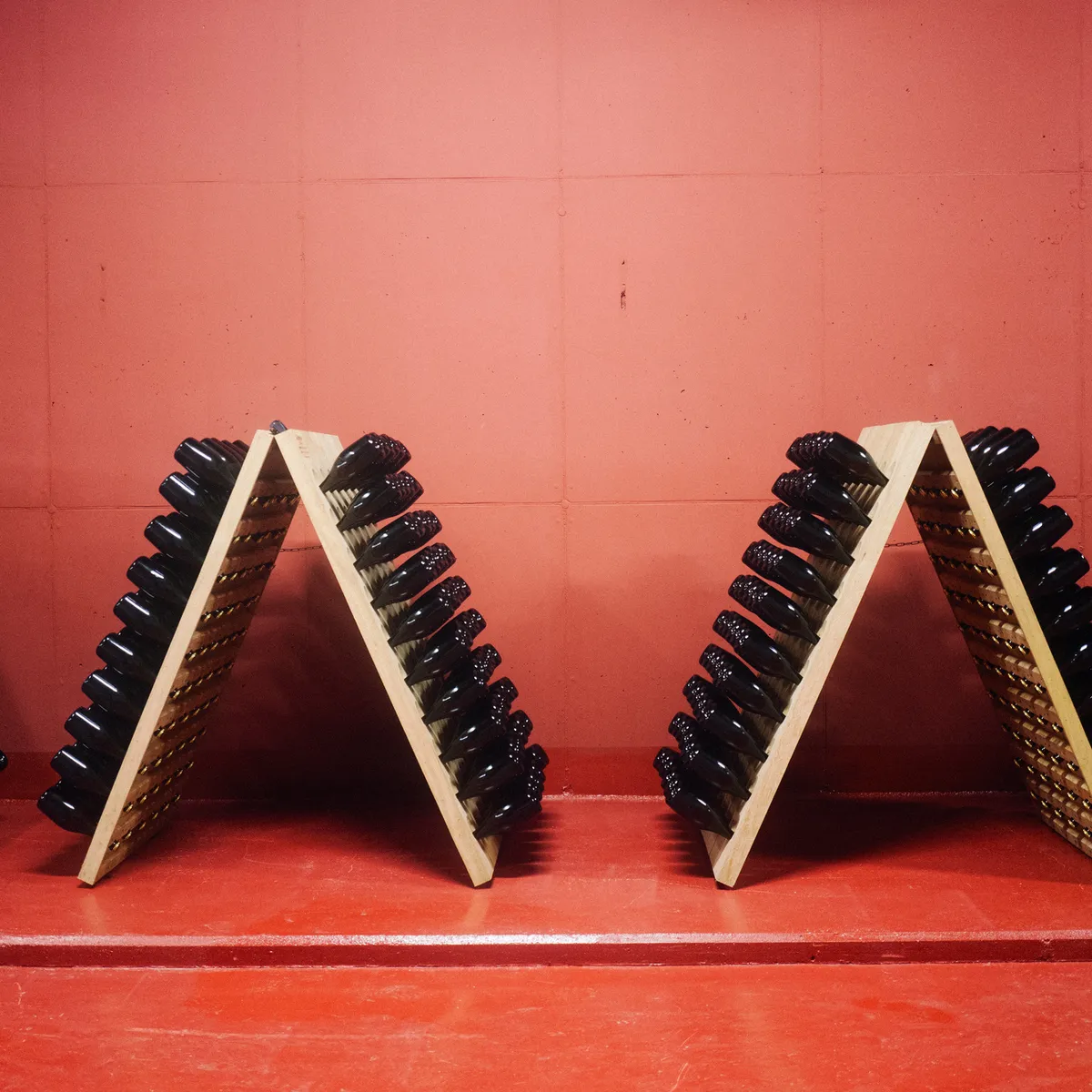 Riddling racks with sparkling wine bottles against a red wall