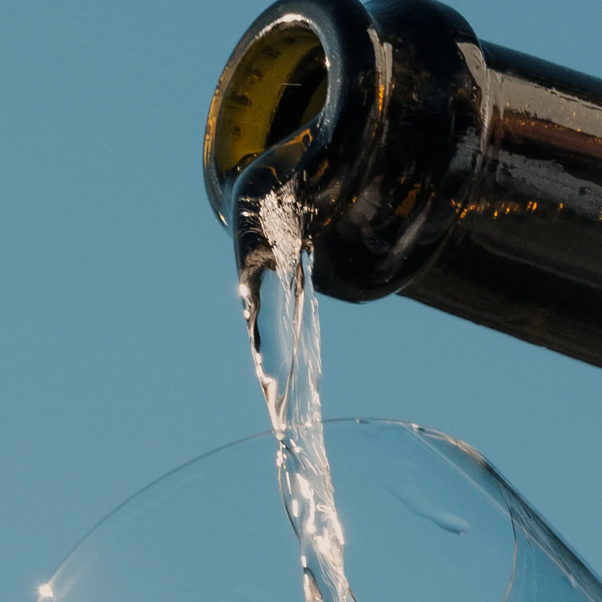 Sparkling wine being poured from the bottle into a glass against a blue sky