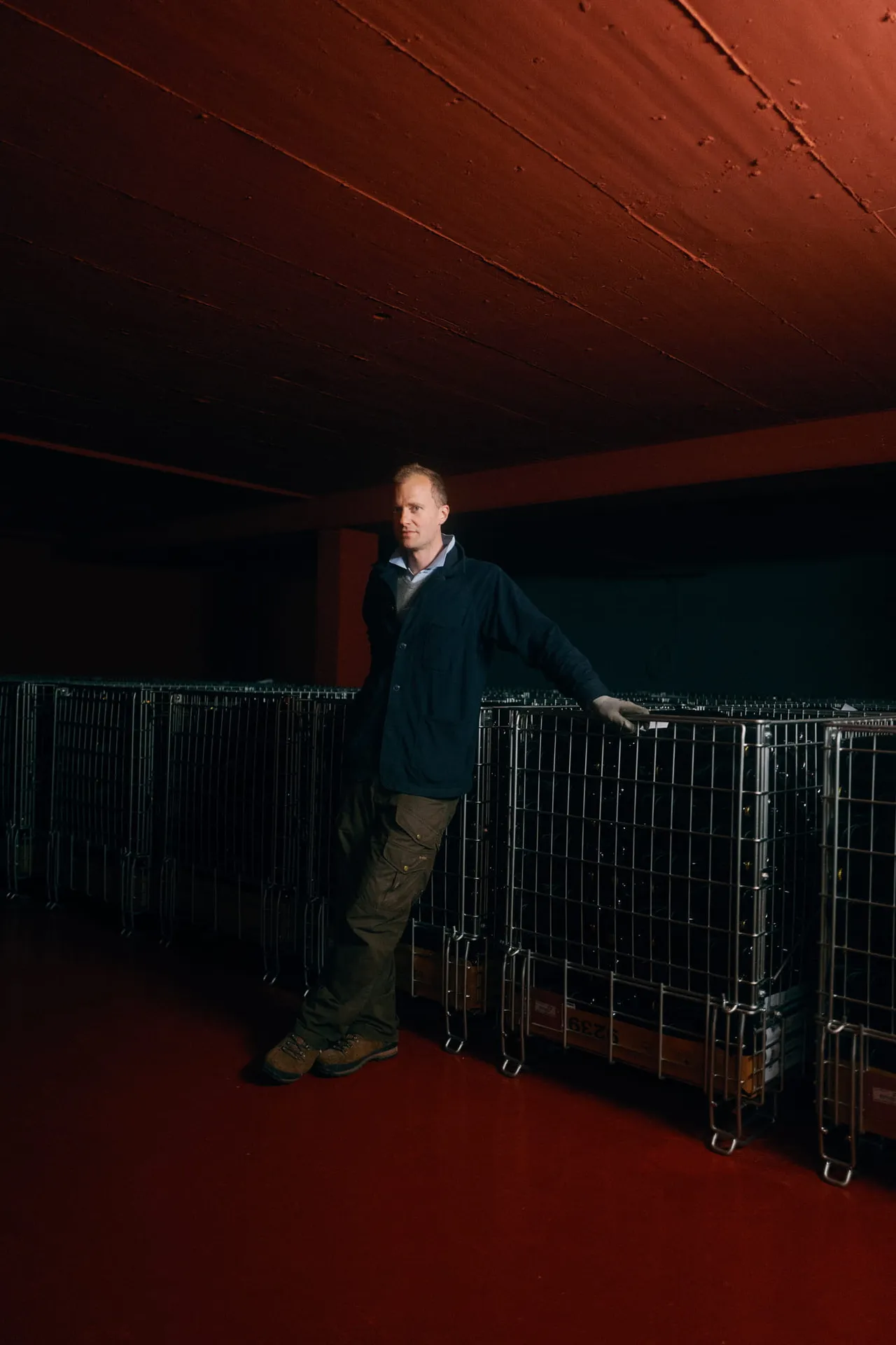 Winemaker leaning against a wire crate of sparkling wine bottles in the cellar